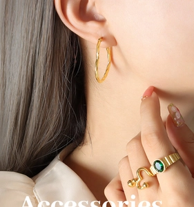 Détail de créoles torsadées dorées et bague avec pierre verte et motifs cœurs