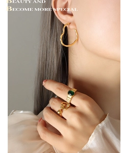 Vue détaillée de créoles cœur dorées et d'une bague avec pierre verte sur un mannequin