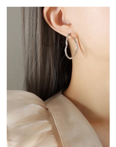 Détail d'une boucle d'oreille créole torsadée argentée sur un mannequin au style pur