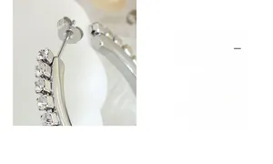 Détail macro de boucles d'oreilles argentées montrant le fermoir papillon et les zircons