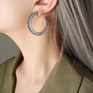 Boucles d'oreilles créoles C en argent avec zircons noirs portées par un mannequin