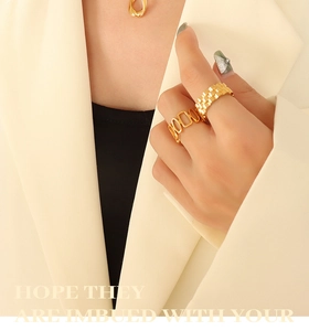 Gros plan de bagues dorées et collier abstrait portés avec un blazer beige chic