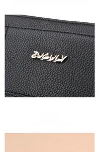 Close-up of black lychee grain leather with a premium gold ZUGULY metal logo on the bag