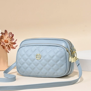 Detail of light blue quilted crossbody bag with golden logo and dual zipper compartments