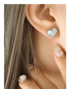 Gros plan de boucles d'oreilles cœur en nacre portées avec bordure argentée ciselée