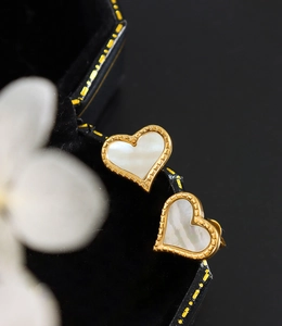 Détail macro de boucles d'oreilles cœur dorées avec nacre blanche et bordure perlée