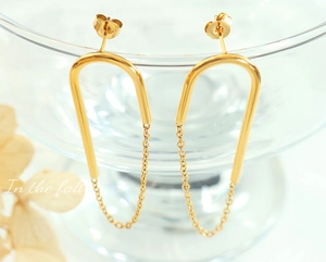 Gros plan de boucles d'oreilles en U avec chaînes dorées sur verre et pétales d'automne