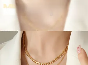 Détail de colliers superposés en or avec maille Figaro portés avec un blazer blanc