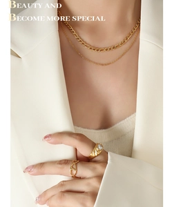 Détail du collier Figaro doré multicouche et des bagues portés avec un blazer blanc