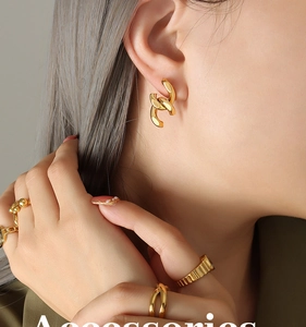 Détail de boucles d'oreilles chaînes dorées entrelacées et bagues texturées sur mannequin