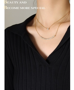 Detail of layered gold smile necklace with zircon pendant on black knitwear