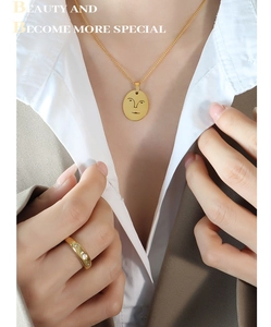 Détail du collier avec pendentif visage doré et de la bague large en or sur un mannequin