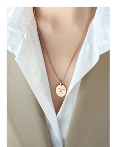 Gros plan d'un collier minimaliste en or rose avec un pendentif visage abstrait ajouré