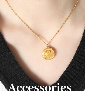 Détail d'un collier pendentif vague doré porté sur un pull en maille noir