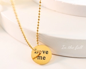 Close-up of golden ball chain necklace with round Love Me engraved pendant on stone