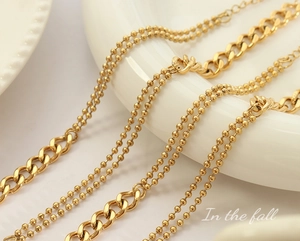 Macro detail of gold-plated layered chain and bead bracelet on a ceramic plate