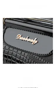 Detail of black crocodile-embossed leather texture with golden Danbaoly logo and hardware