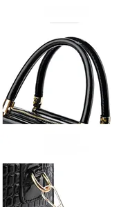 Detail of glossy black crocodile pattern handbag with golden metal hardware and round handles