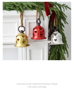 Close-up of three festive metal bells with hollow heart patterns on a fireplace