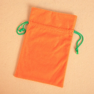 Orange velvet Halloween drawstring gift bag with green cord on beige felt background