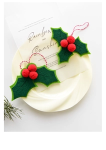 Macro shot of green felt holly leaf Christmas ornament with red pom poms on cream plate