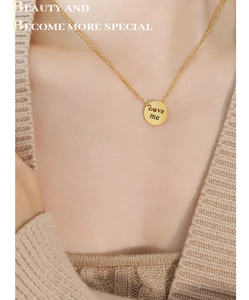Golden round pendant necklace with Love me engraving worn on a beige knit sweater