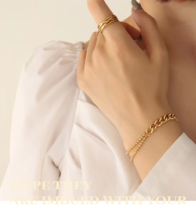 Detail of layered gold titanium steel chain bracelet and crisscross ring for women