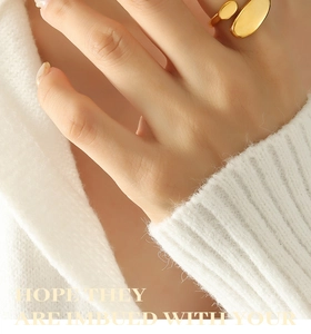 Close-up of gold-plated minimalist oval ring worn by model over a knit background