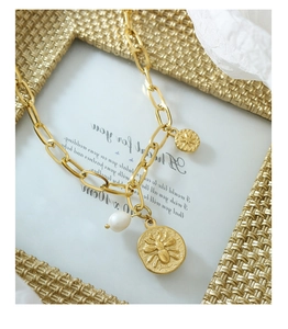 Detailed shot of a vintage gold steel necklace with bee coin, star charm and pearl drop