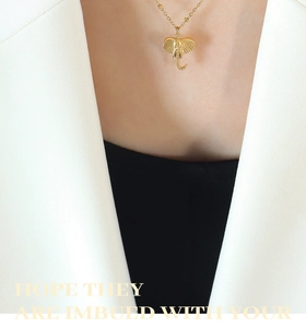 Close-up of a tiny golden elephant pendant necklace on model wearing a white suit