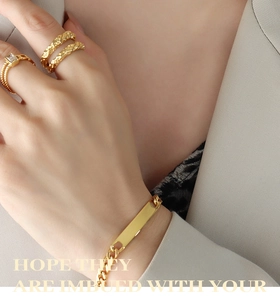 Detail of gold Cuban chain bracelet with nameplate and textured zircon ring set on model
