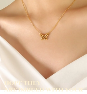 Detailed close-up of a golden butterfly necklace with a textured beaded pendant design