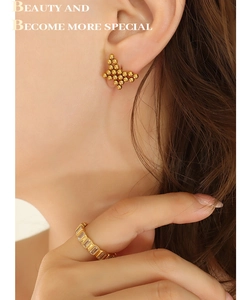 Detail of golden beaded butterfly earrings and rectangle zircon ring on a model