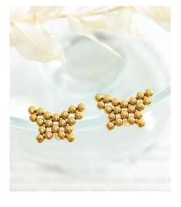 Macro shot of gold butterfly stud earrings made of tiny metallic beads on glass edge