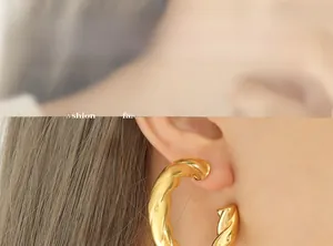 Close-up of model wearing large golden twisted hoop earrings in titanium steel