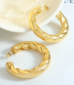 Macro detail of textured gold C-shape hoop earrings with a twisted metallic finish