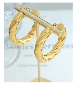 Close-up of golden hollow twisted rope hoop earrings displayed on a minimalist gold stand