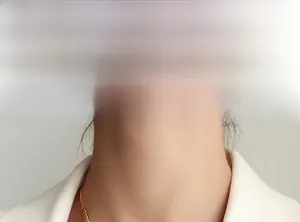 Gros plan d'un collier chaîne gourmette dorée porté par un mannequin en blazer blanc
