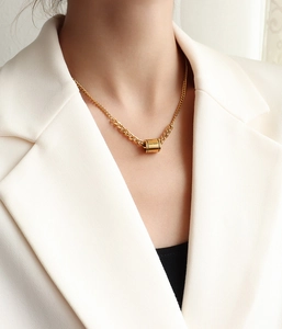 Détail d'un pendentif tube doré avec gravure 'follow your heart' sur une chaîne à maillons