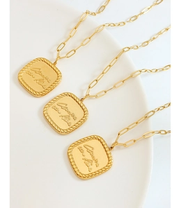 Detail of square gold pendants with cursive engraving and rope border on white ceramic