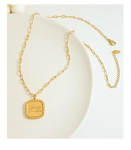 Detail of 18K gold-plated paperclip chain necklace with engraved square pendant on ceramic tray