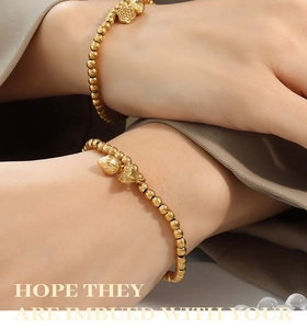 Detailed view of gold-plated beaded bracelet with lotus pendant on wrist over grey fabric
