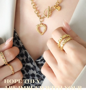 Close-up of gold OT buckle heart necklace and stacked rings on female model