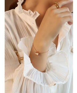 Detail of rose gold barrel charm bracelet on wrist with elegant rings and white shirt