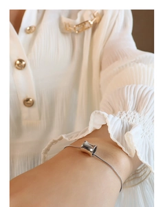 Close-up of a silver-toned snake chain bracelet with a polished cylindrical charm on wrist