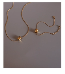 Detailed view of gold snake chain jewelry set with concave cylindrical tube pendants