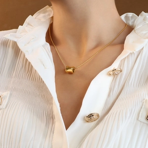 Polished 18K gold cylinder pendant necklace on fine snake chain worn by a female model