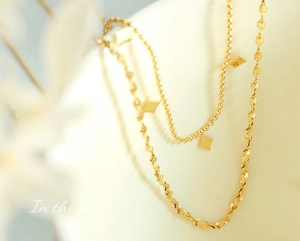 Detail of gold double-layer necklace featuring rhombus pendants and textured chain links