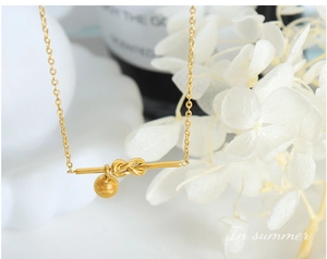 Close-up of golden necklace featuring minimalist knot detail and hanging bead pendant