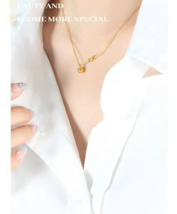 Close-up of a gold-plated necklace featuring a knot pendant and round bead on a model